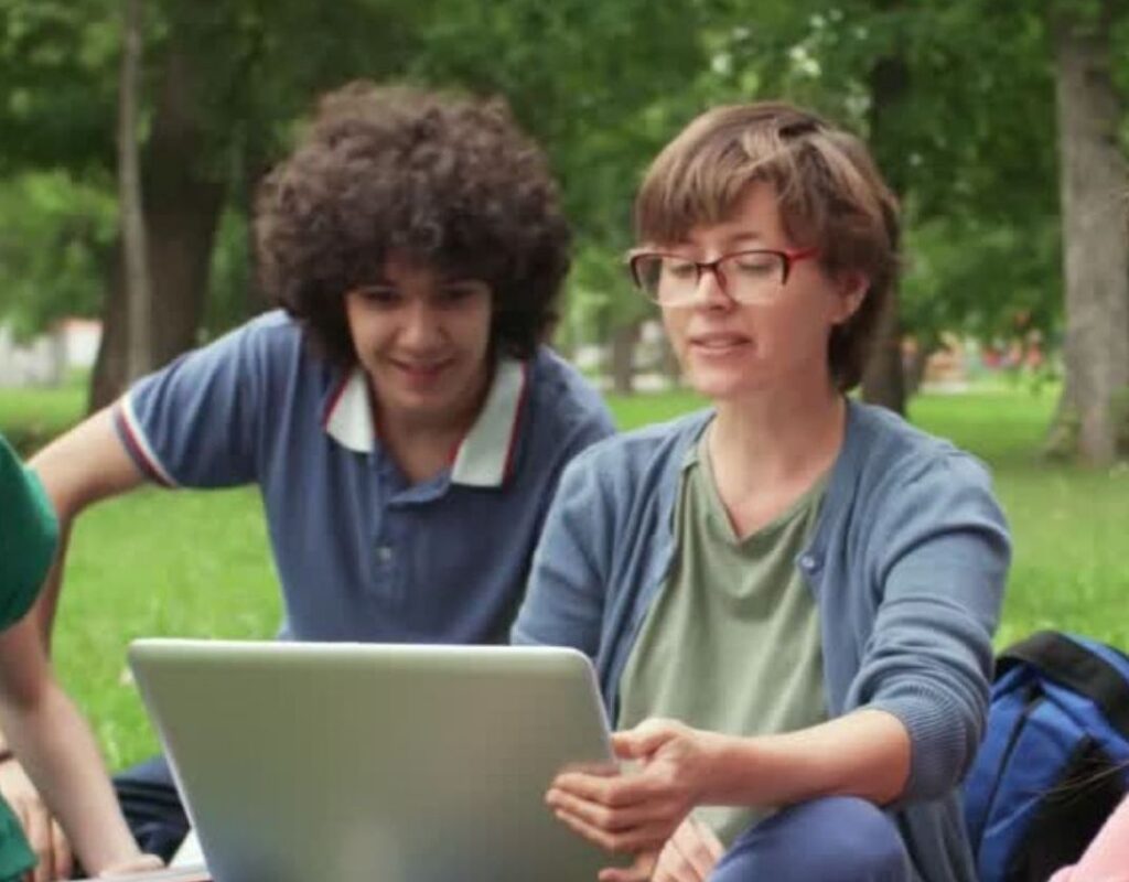 two young people sitting outside in a park, looking at a laptop
