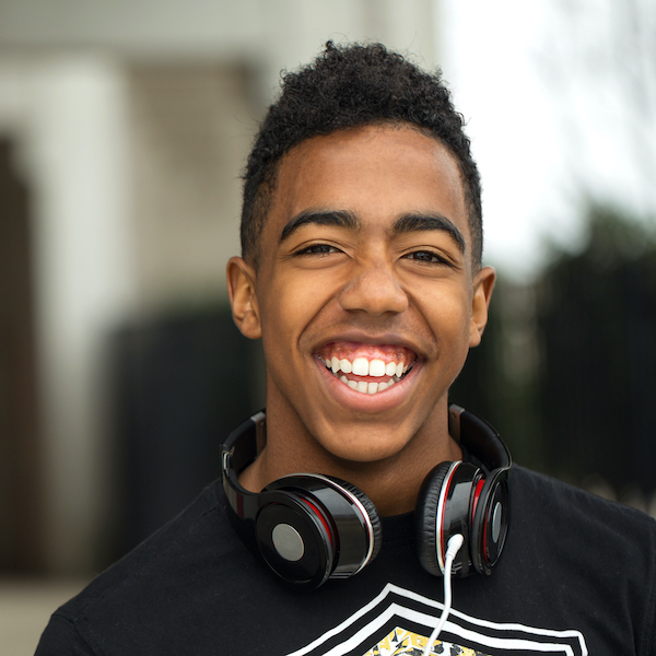 Young man smiling, looking at the camera, headphones around his neck