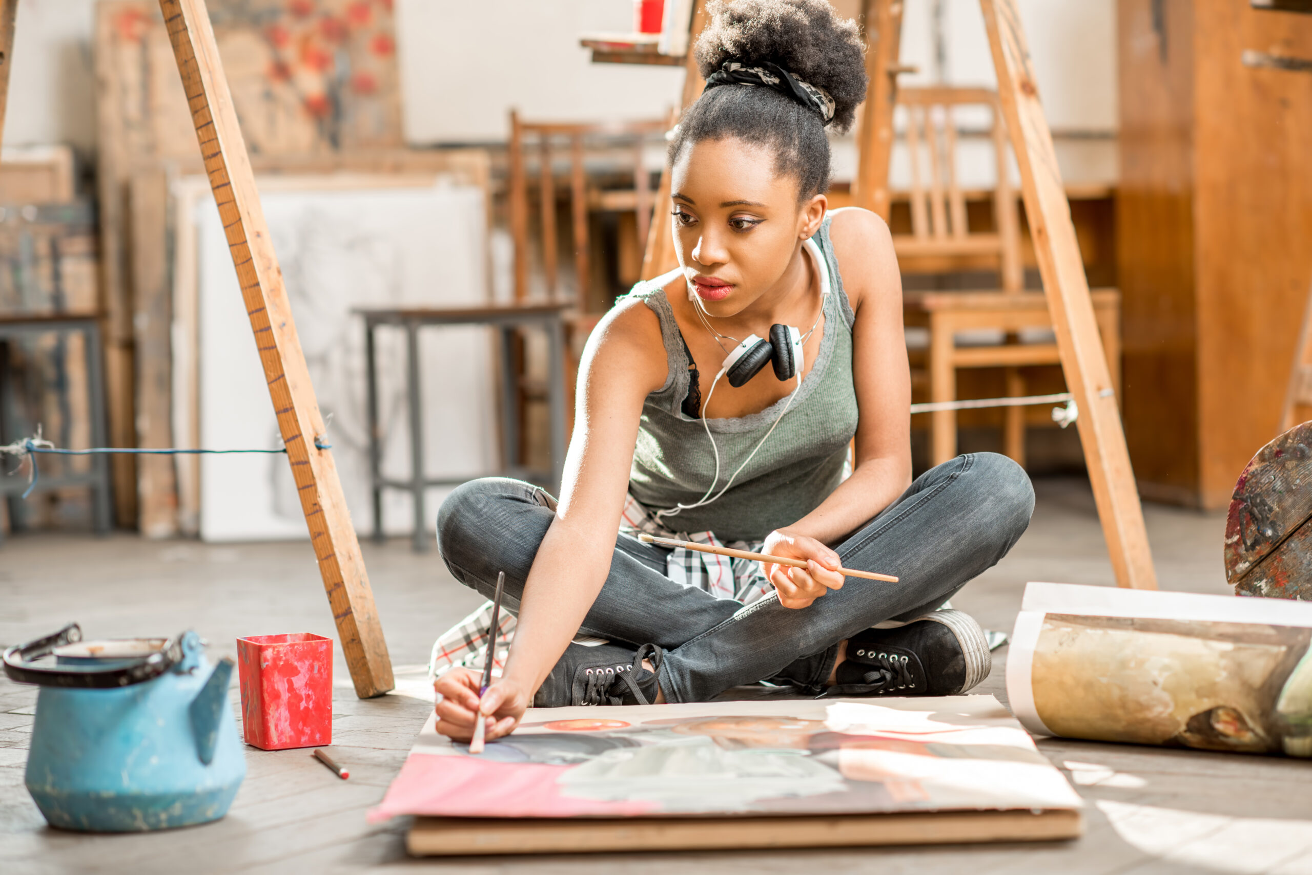 young woman sitting cross legged on the floor of an art studio, painting